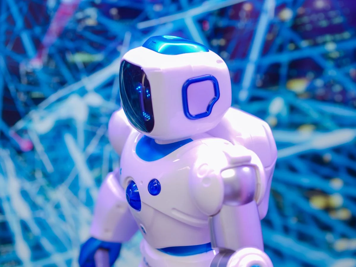 青い光の背景に立つ小さなロボット。「AIガバナンスとは」の話題のイメージ