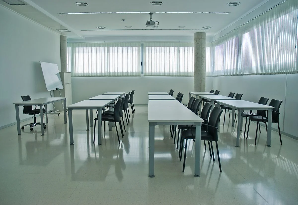 白い机と椅子が並ぶ無人の研修室。「社内PMOを育てる前提で頼めるか」の話題のイメージ