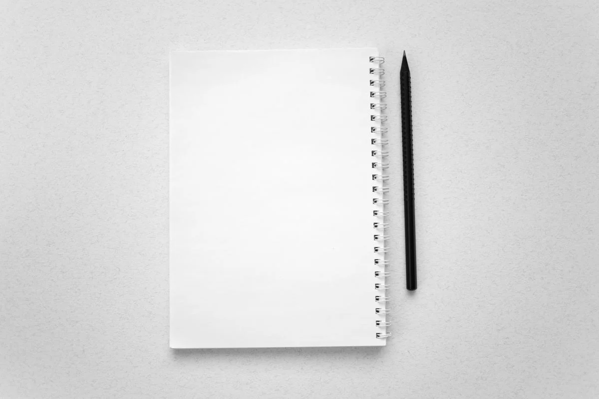 白紙のスパイラルノートと黒い鉛筆。並行稼働の期間に手順を書き残す話題のイメージ